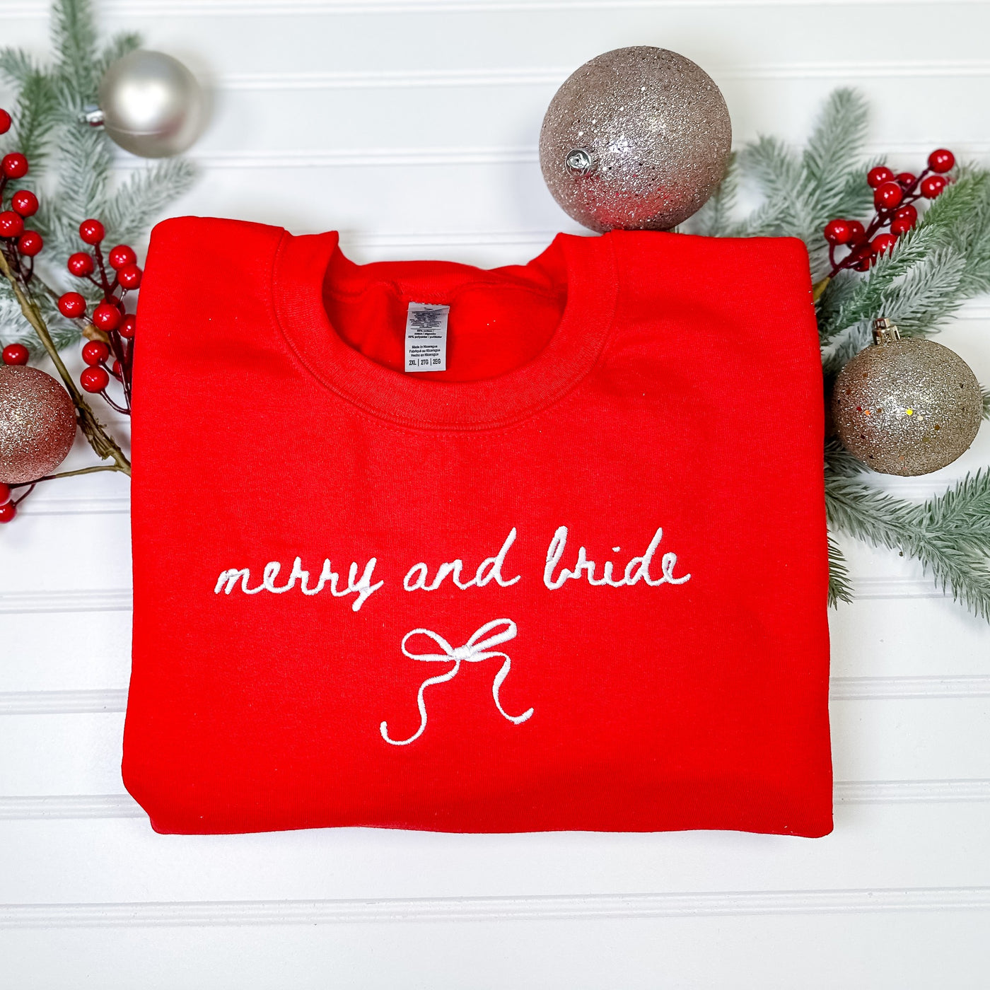 A red crewneck sweatshirt features delicate white embroidered details and a bow design, perfect for a festive bridal occasion.