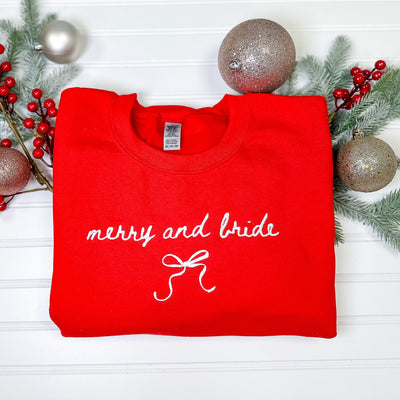 A red crewneck sweatshirt features delicate white embroidered details and a bow design, perfect for a festive bridal occasion.