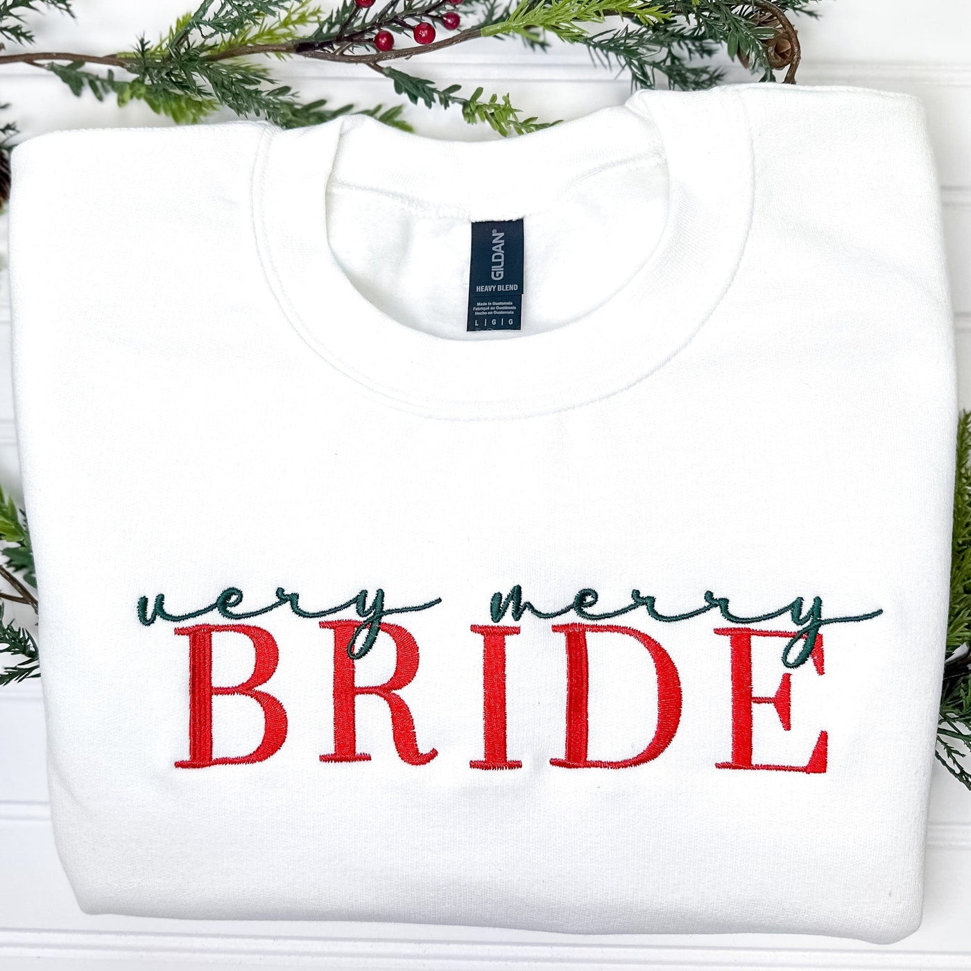 A white crew neck sweatshirt featuring festive red and green embroidery, suitable for a holiday bridal event.