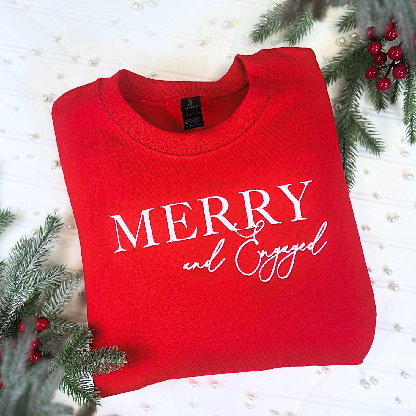 A festive red crewneck sweatshirt made of soft fabric, featuring a white graphic celebrating an engagement, perfect for holiday wear.