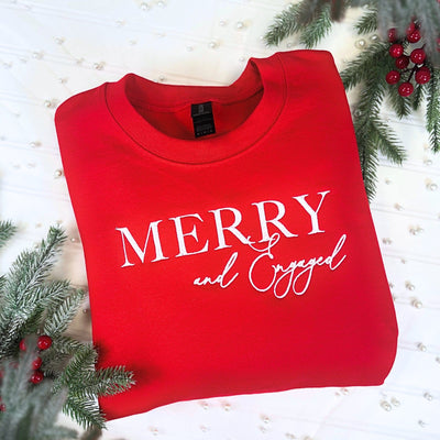 A festive red crewneck sweatshirt made of soft fabric, featuring a white graphic celebrating an engagement, perfect for holiday wear.
