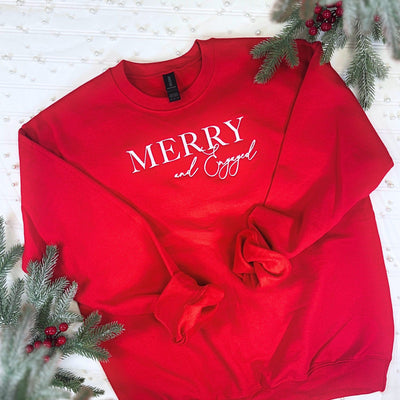 A vibrant red crewneck sweatshirt crafted from a soft fabric, featuring a white graphic design for a winter engagement or holiday celebration, displayed with frosted evergreen branches.