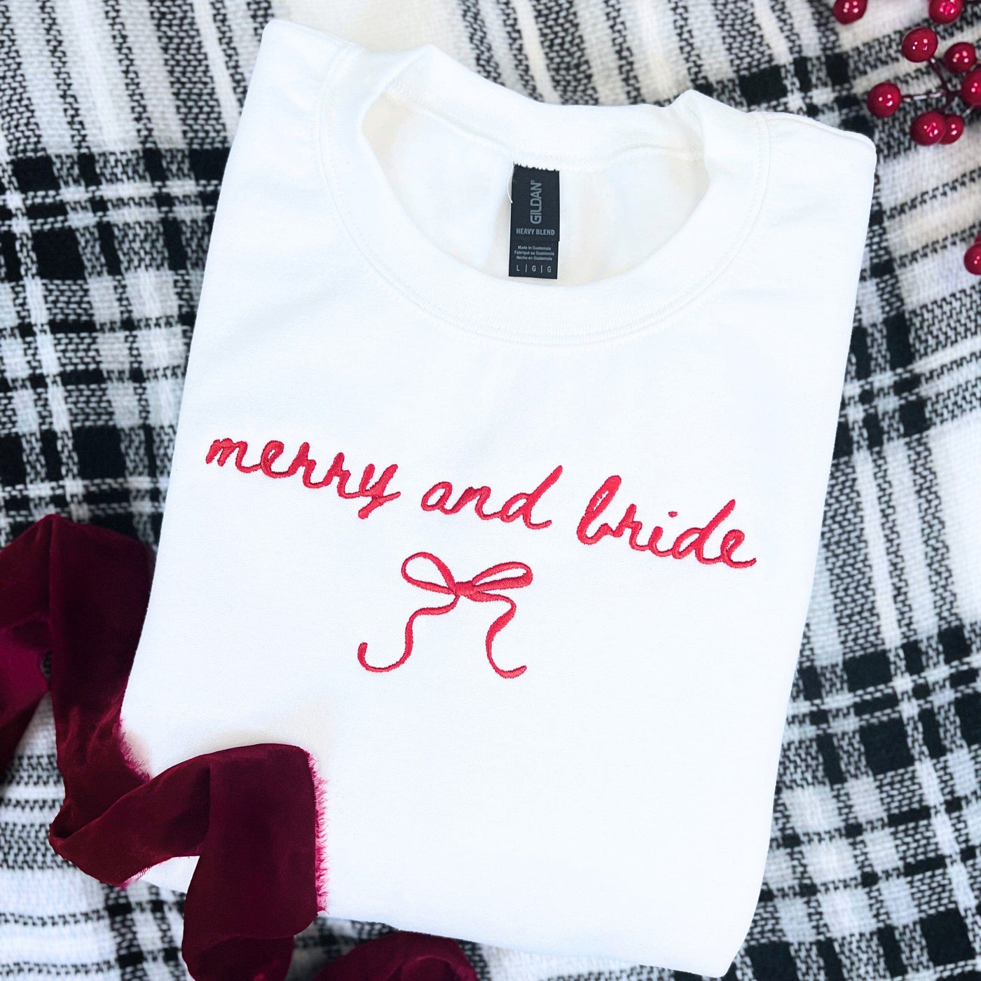 A white crewneck sweatshirt featuring red embroidered lettering and a bow design, suitable bridal apparel for a festive wedding occasion.