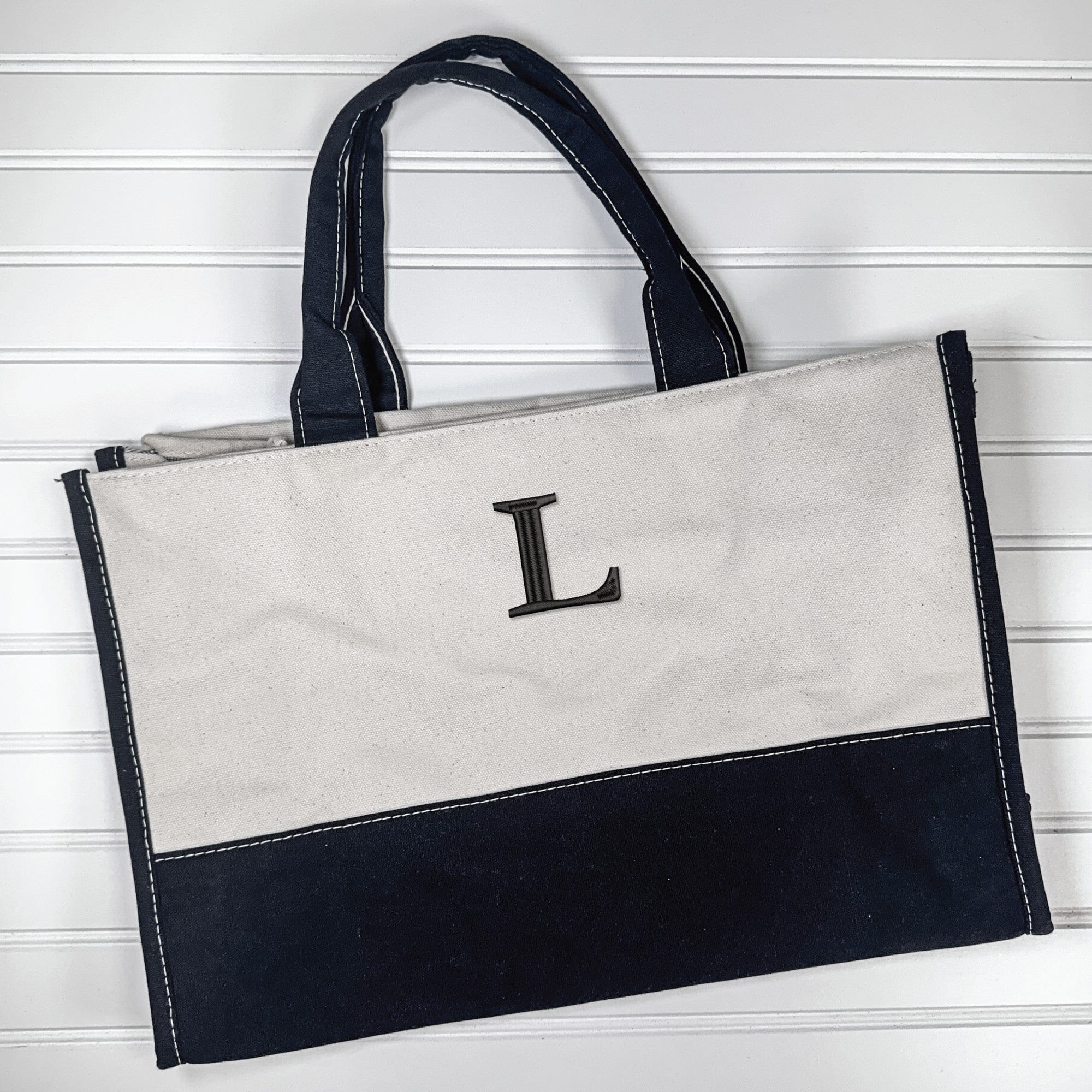 A two-tone canvas tote bag in light and dark navy, with sturdy handles and white contrast stitching, designed as a personalized accessory for a wedding or event.