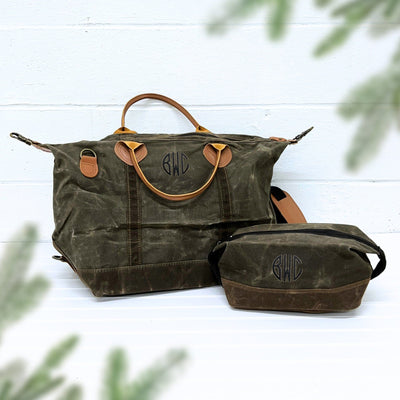A two-piece set featuring a dark green waxed canvas duffel bag and a matching toiletry bag with tan leather accents, perfect for personalized travel or as a wedding party gift.