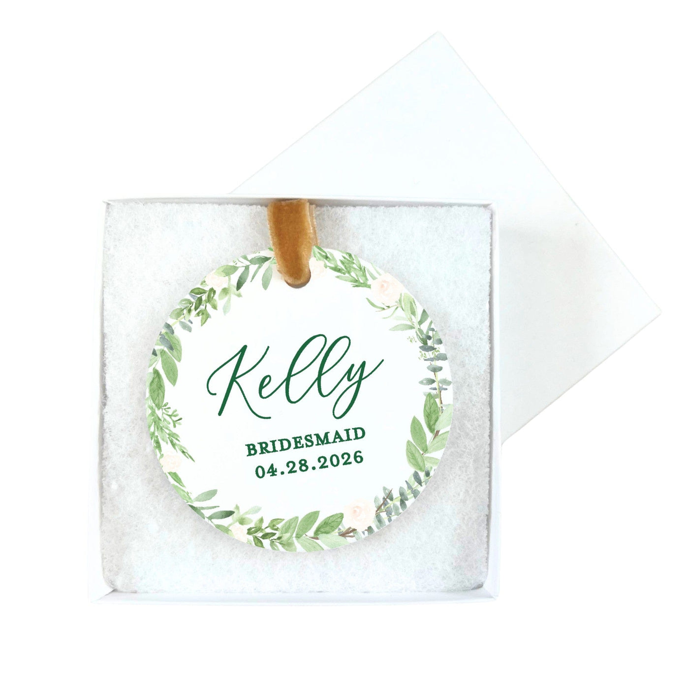 A circular white tag featuring a watercolor green foliage and light pink floral wreath design, attached to a brown velvet ribbon, serving as a personalized wedding or bridal shower favor or gift tag.