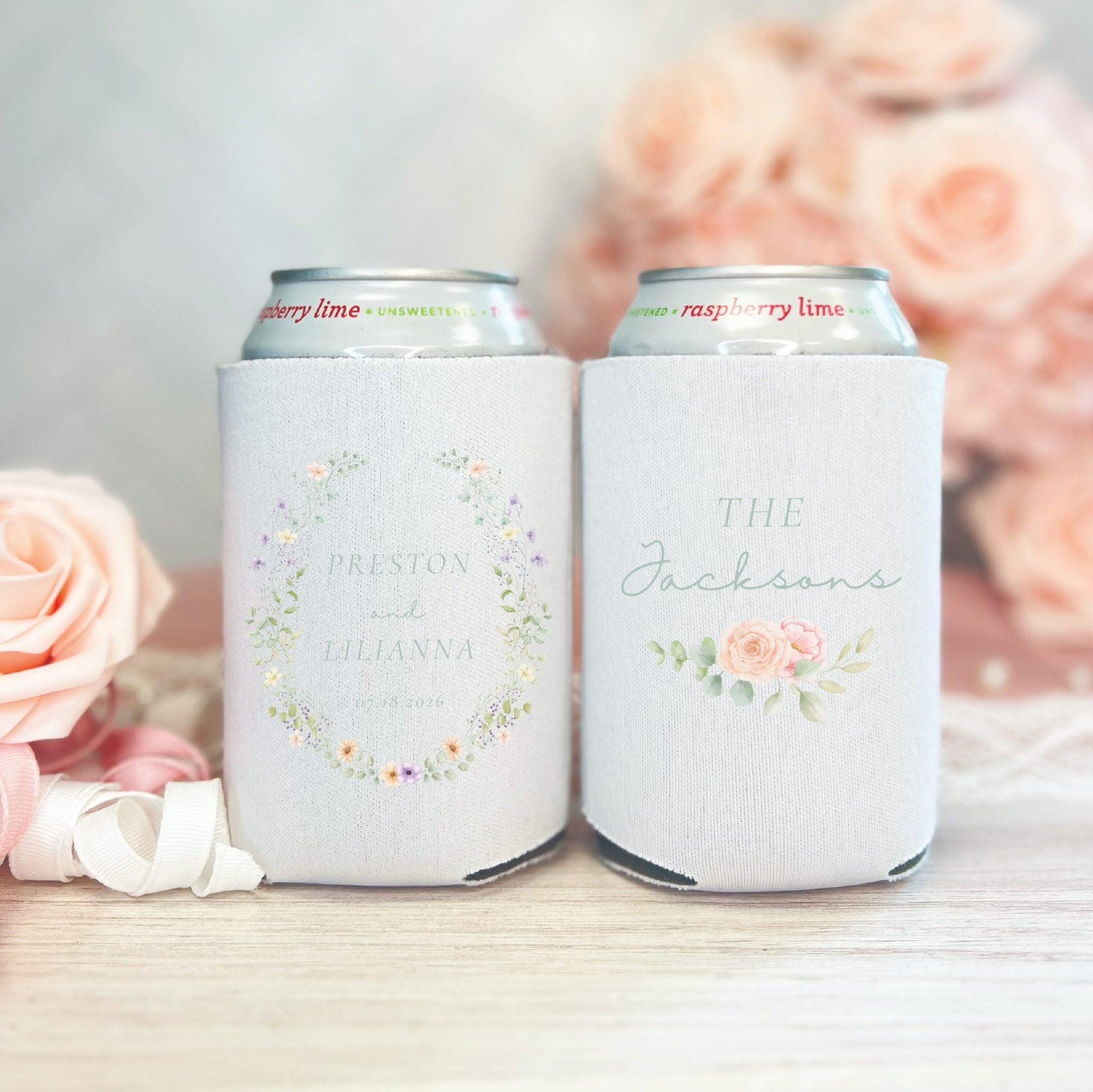 Two white can coolers with personalized wedding designs, one with floral wreath and names, the other with roses and "The Jacksons" text