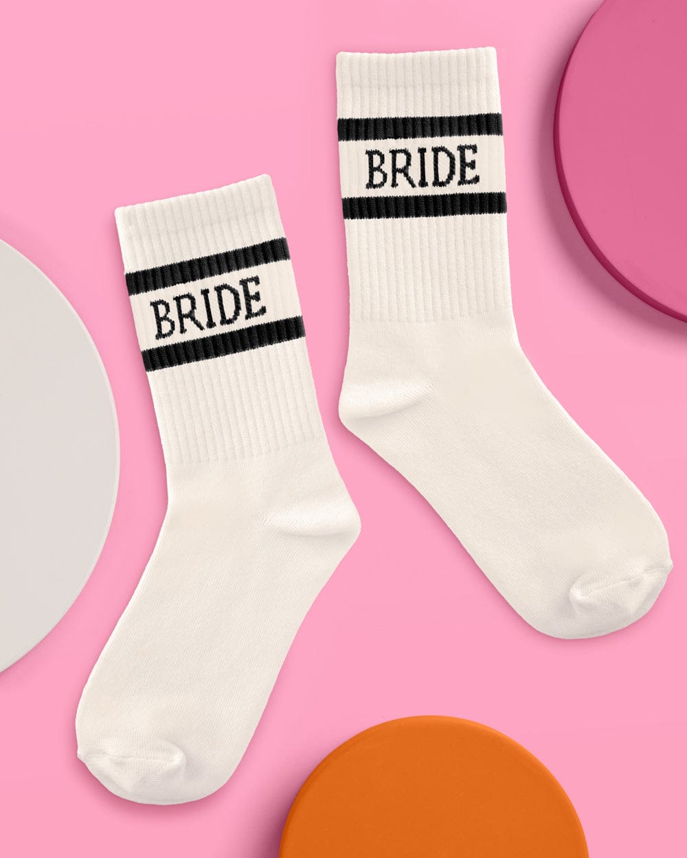 Pair of ivory tube socks with black stripes and "BRIDE" text, displayed on pink background