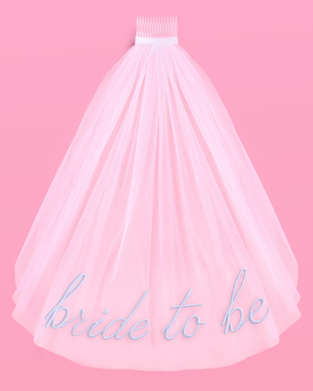 Pink tulle veil with "bride to be" embroidered in blue script across the skirt, white comb at top, on pink background.