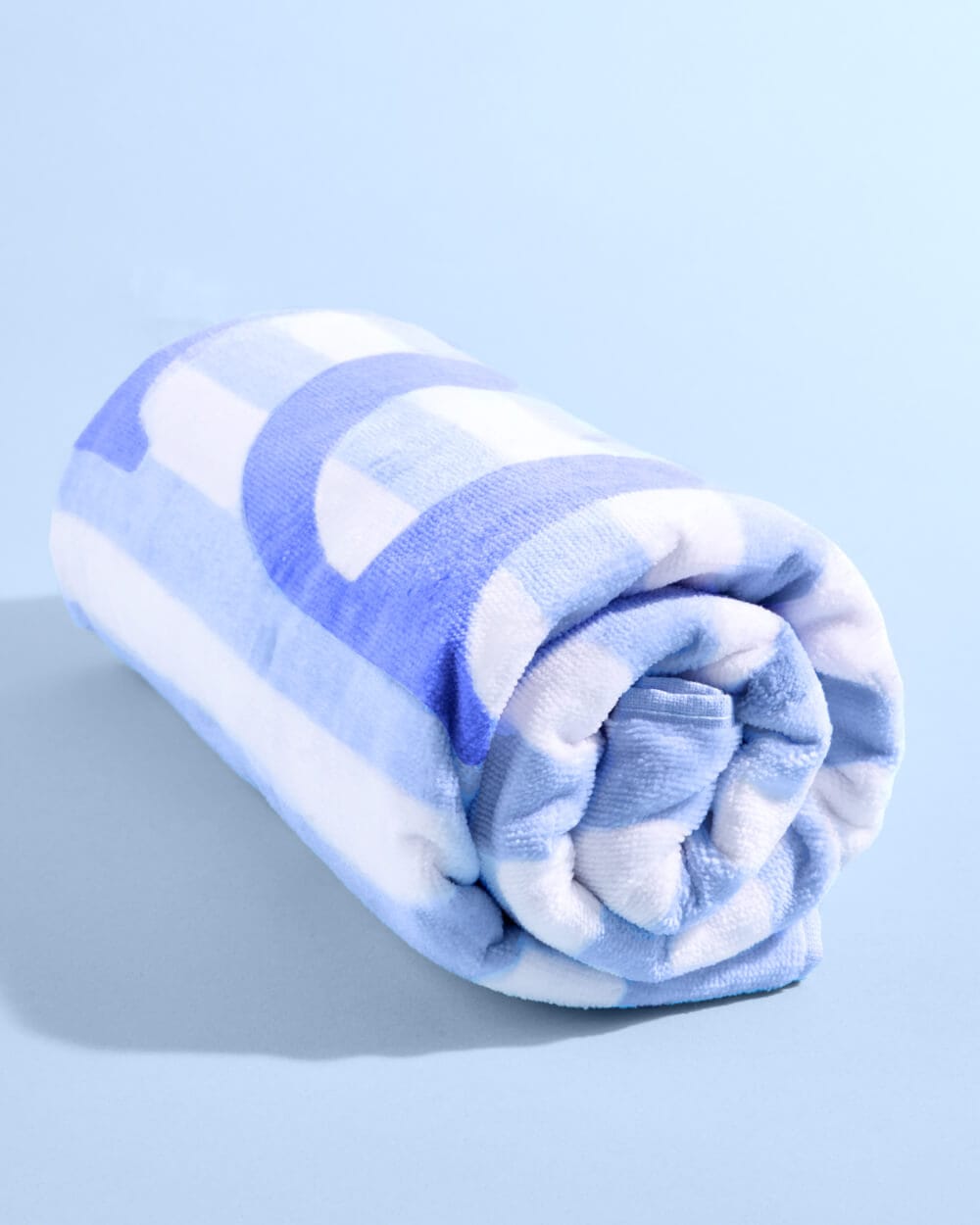 Blue and white striped cotton beach towel rolled up on light blue background