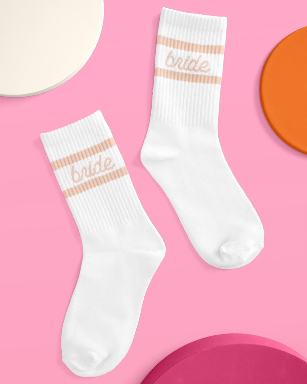 Pair of white crew socks with beige and pink striped cuff and "bride" text design on pink background