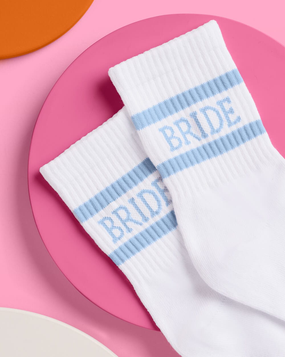 Pair of white crew socks with light blue stripes and "BRIDE" text on a pink circular background.