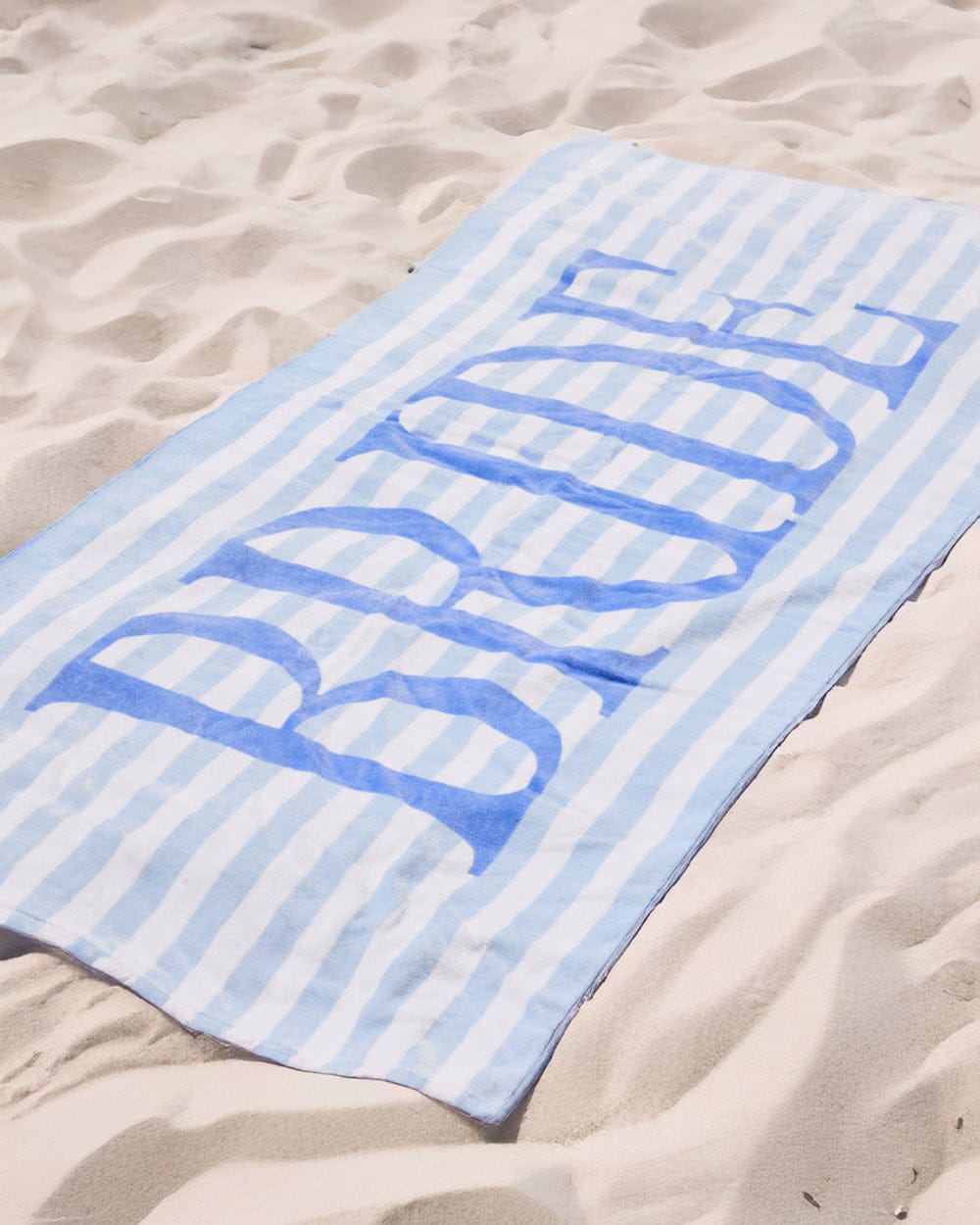 Blue and white striped beach towel with "Bride" text in large letters, laid on sand.