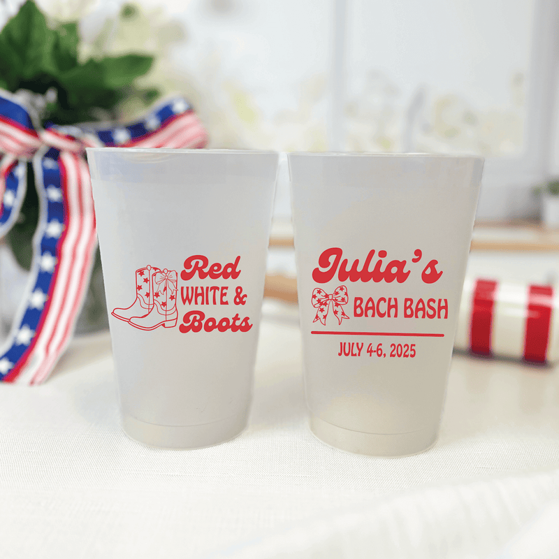 Two frosted cups with red text: left cup reads "Red White & Boots" with cowboy boot design, right cup reads "Julia's Bach Bash July 4-6, 2025"