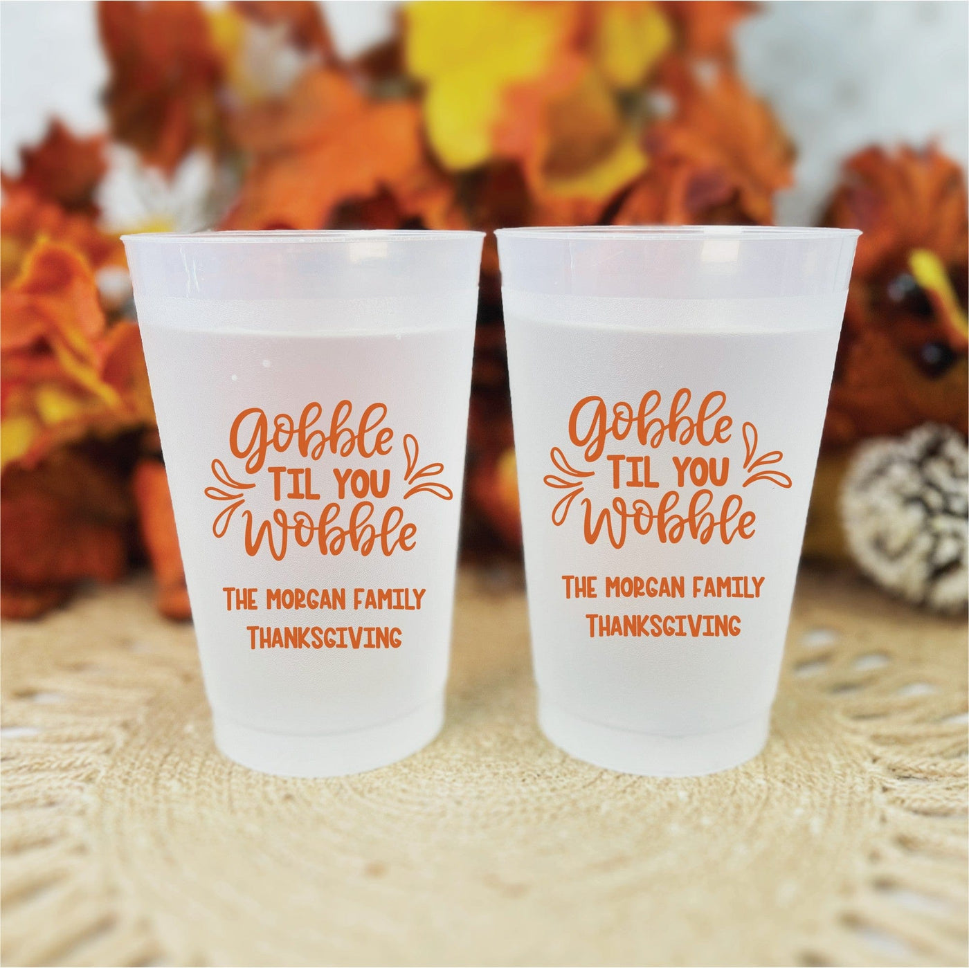 Two frosted plastic reusable cups, each decorated with a personalized orange design, ideal for a Thanksgiving celebration.