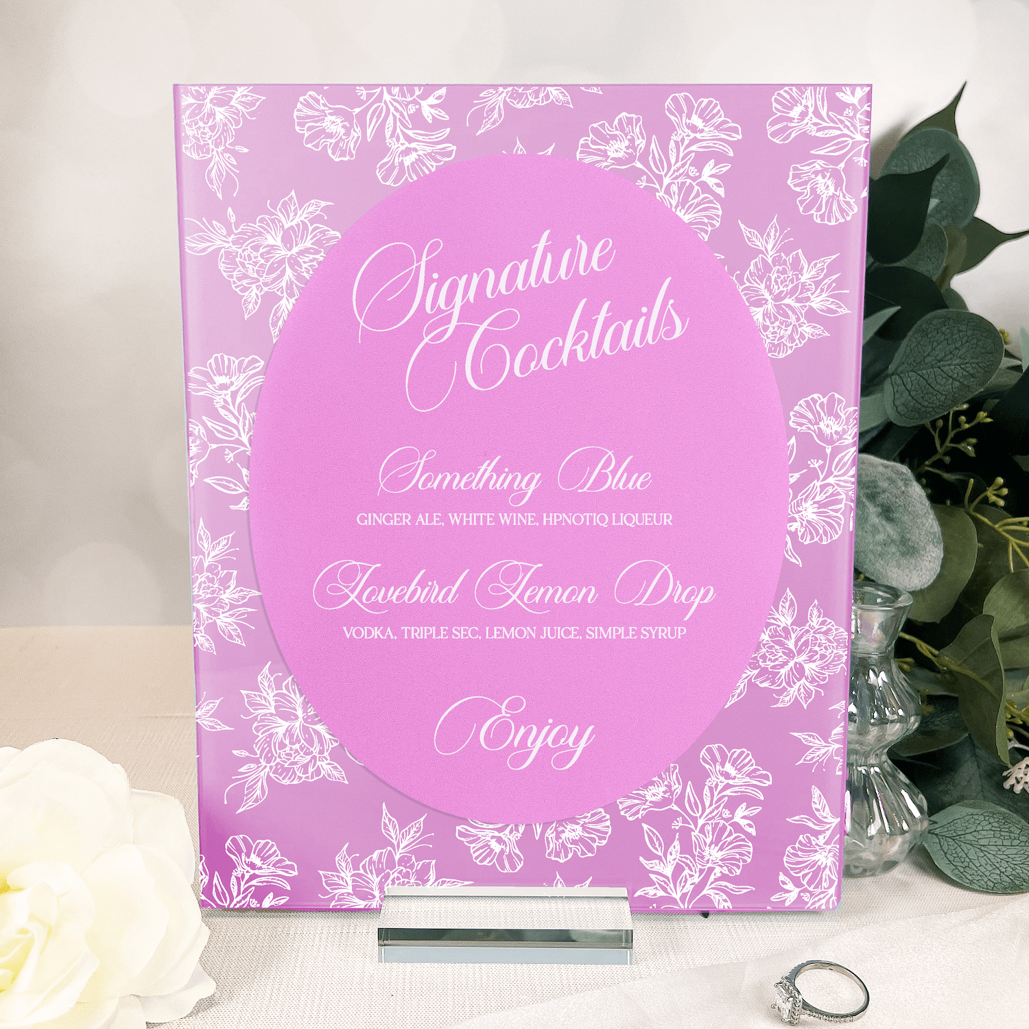 Bright pink acrylic sign with white floral toile border and elegant script text listing signature cocktails and drink descriptions