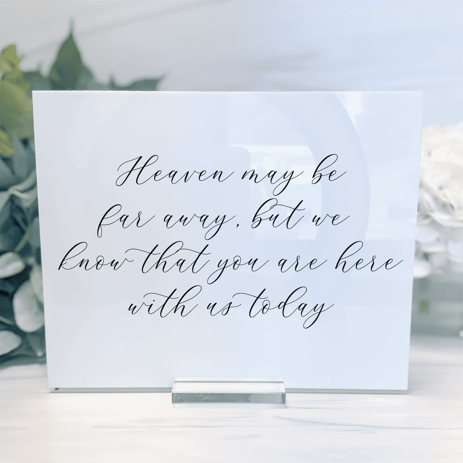 White acrylic memorial sign with cursive script reading "Heaven may be far away, but we know that you are here with us today"