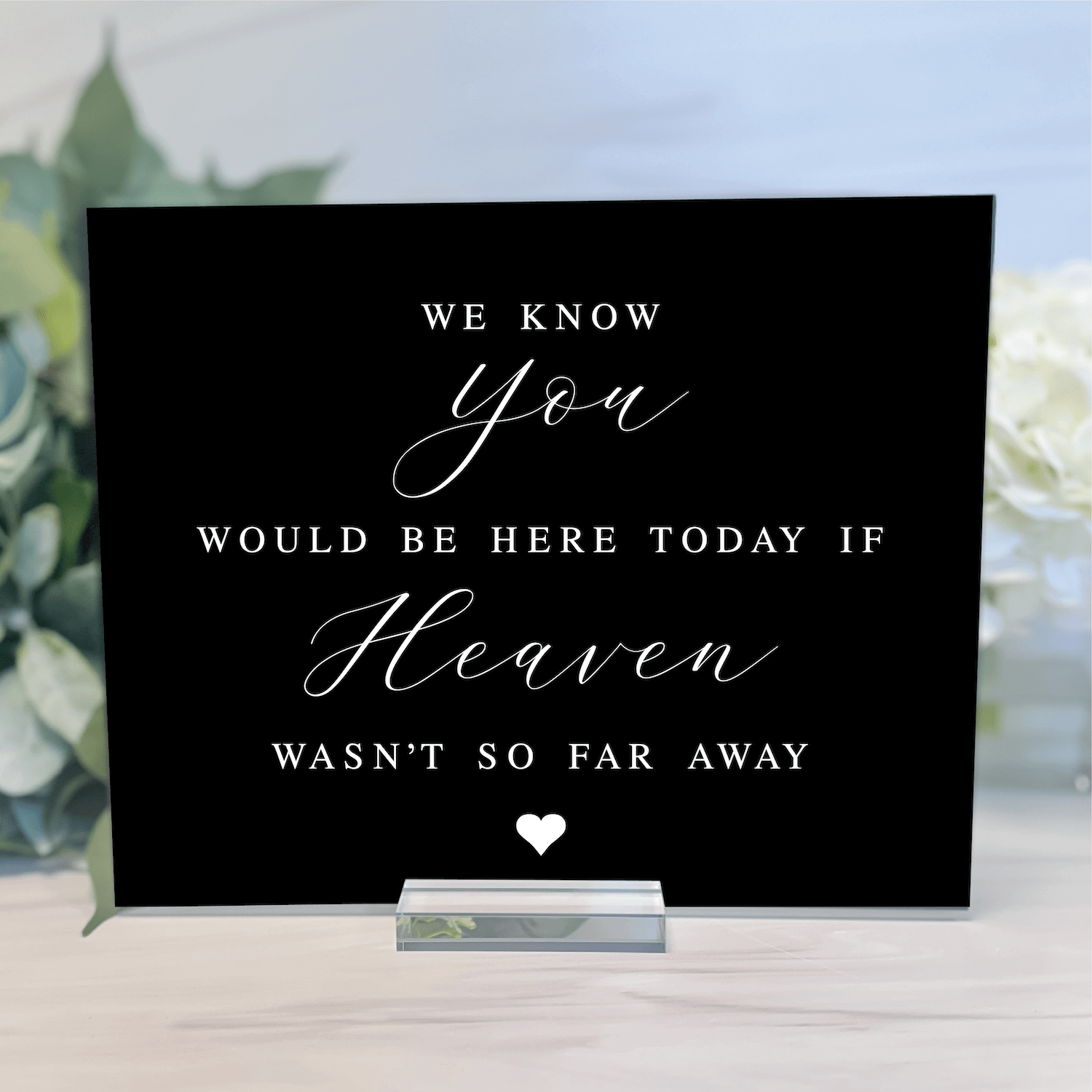 Black acrylic memorial sign with white script and block text reading "We know you would be here today if Heaven wasn't so far away" with small heart, displayed on silver stand