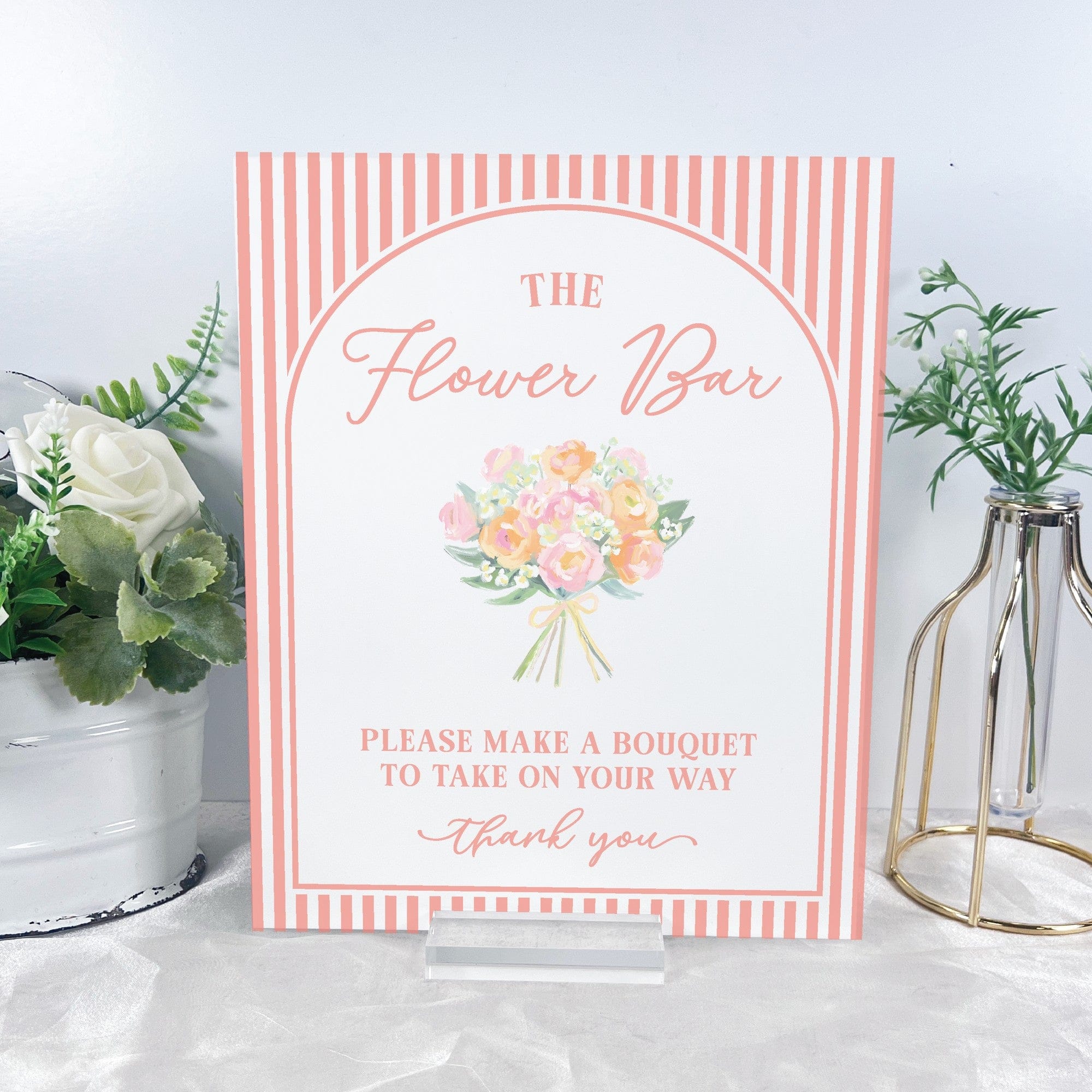 A rectangular table sign with a peach and white striped border, featuring a watercolor illustration of a pastel floral bouquet in the center and displayed on a clear acrylic stand, perfect for a wedding or event flower bar.
