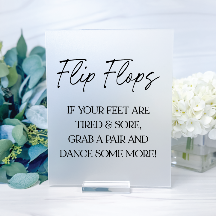 Frosted rectangular acrylic wedding flip flop sign with black lettering inviting guests to grab a pair and dance some more at the reception.