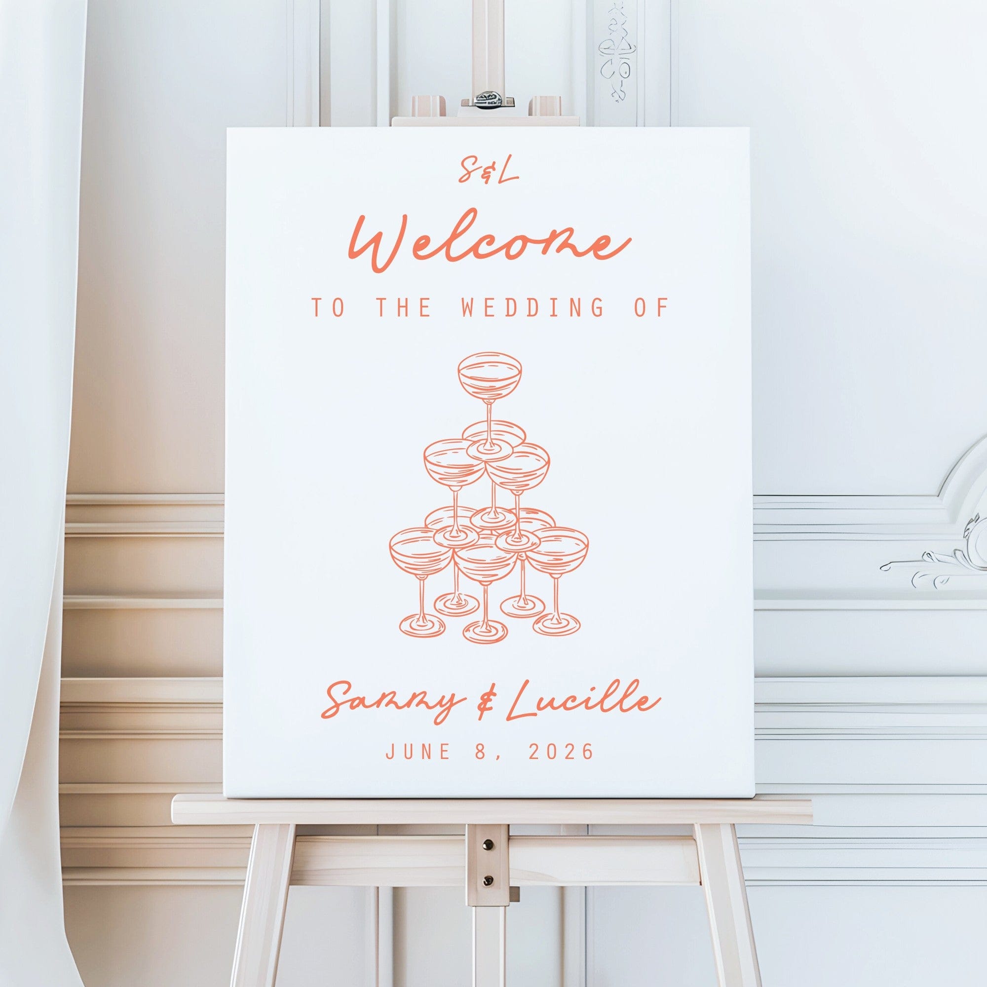 A white personalized wedding welcome sign featuring elegant coral lettering and an illustration of a champagne coupe tower, displayed on a wooden easel to greet guests at an event.