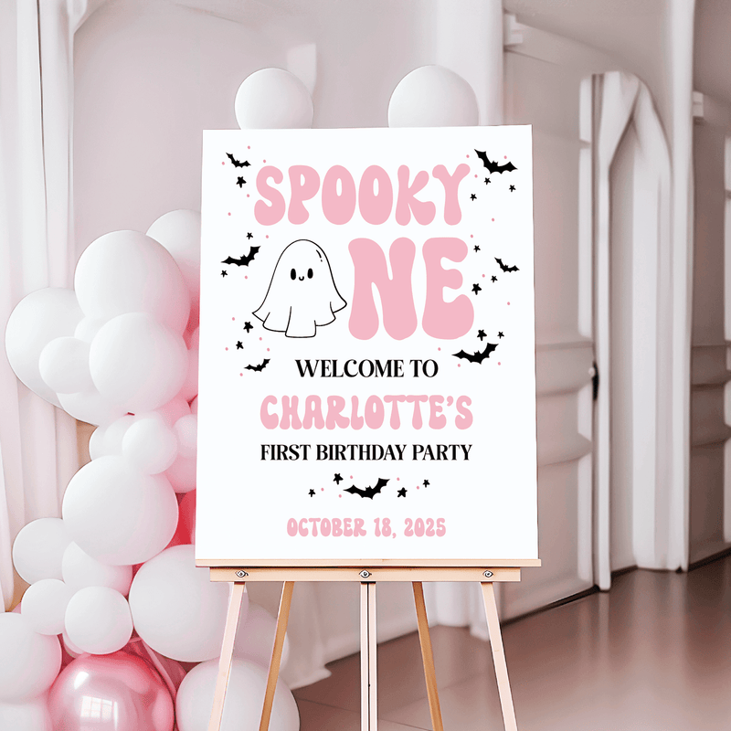 White welcome sign with pink "Spooky One" text, ghost and bat illustrations, personalized with name and date for first birthday party