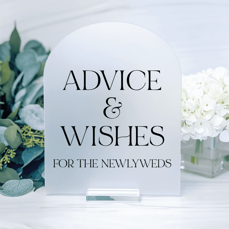 White acrylic arch sign with "Advice & Wishes for the Newlyweds" text, displayed on table with white flowers and greenery.