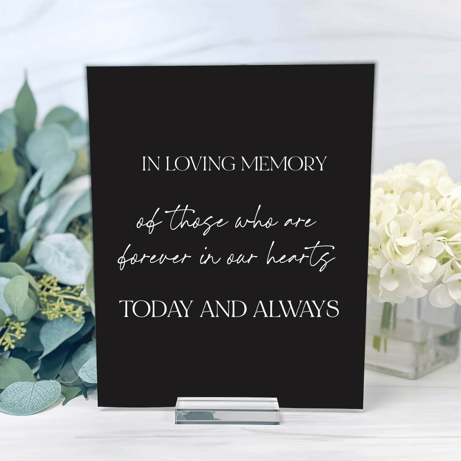 Black acrylic memorial sign with white text reading "In Loving Memory" and "Today and Always" surrounded by white flowers and greenery.