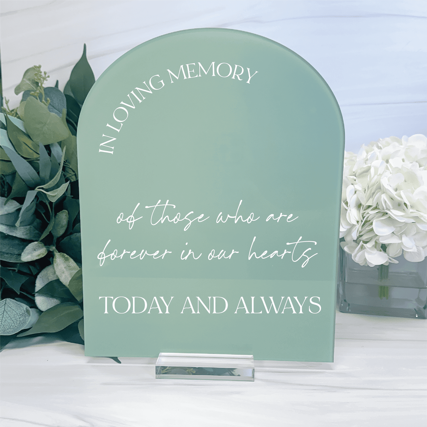 Sage green arched acrylic sign with "In Loving Memory" and "Today and Always" text, displayed with white flowers and greenery.