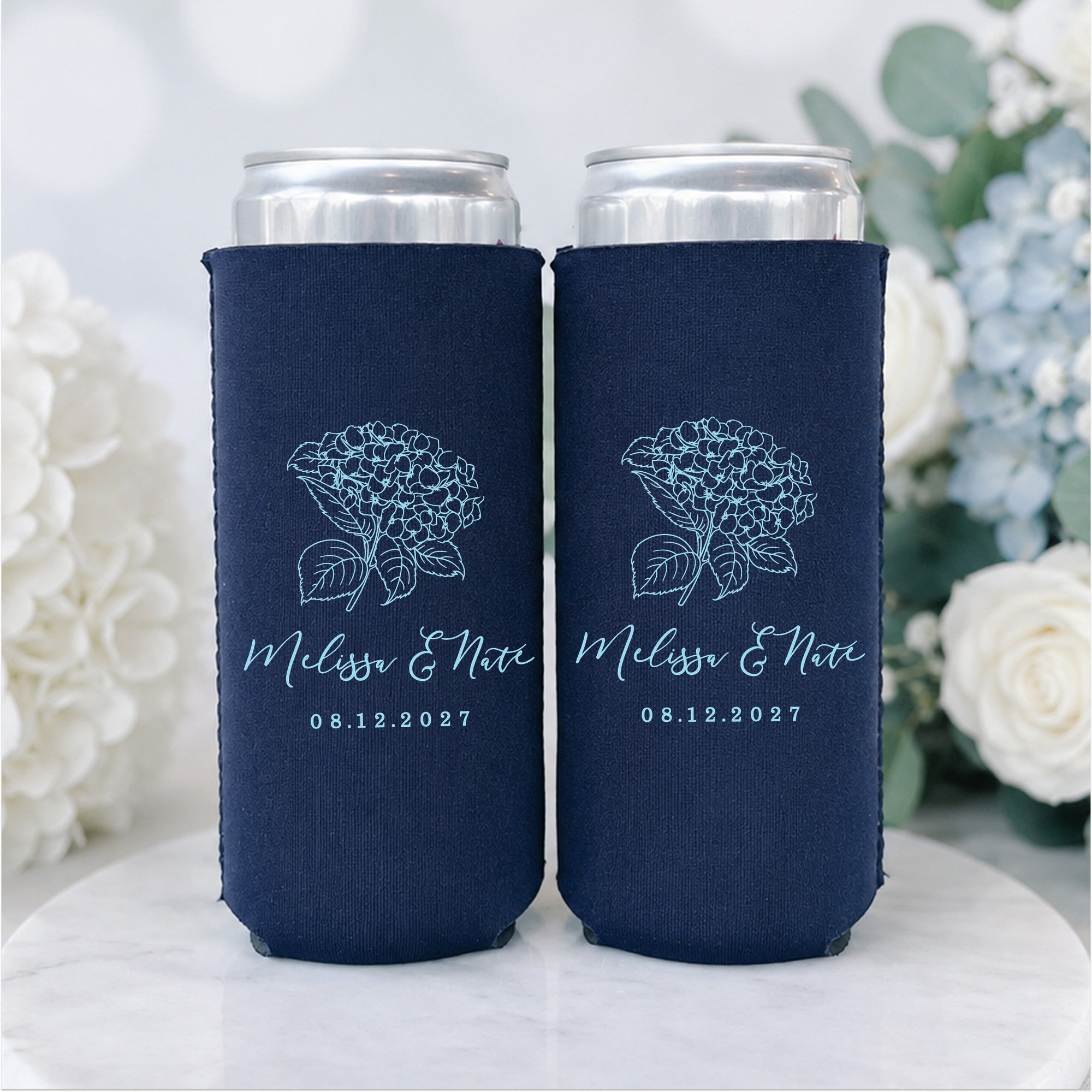Two navy blue foam slim can coolers, each featuring a light blue outline of a hydrangea flower, designed as personalized wedding favors.
