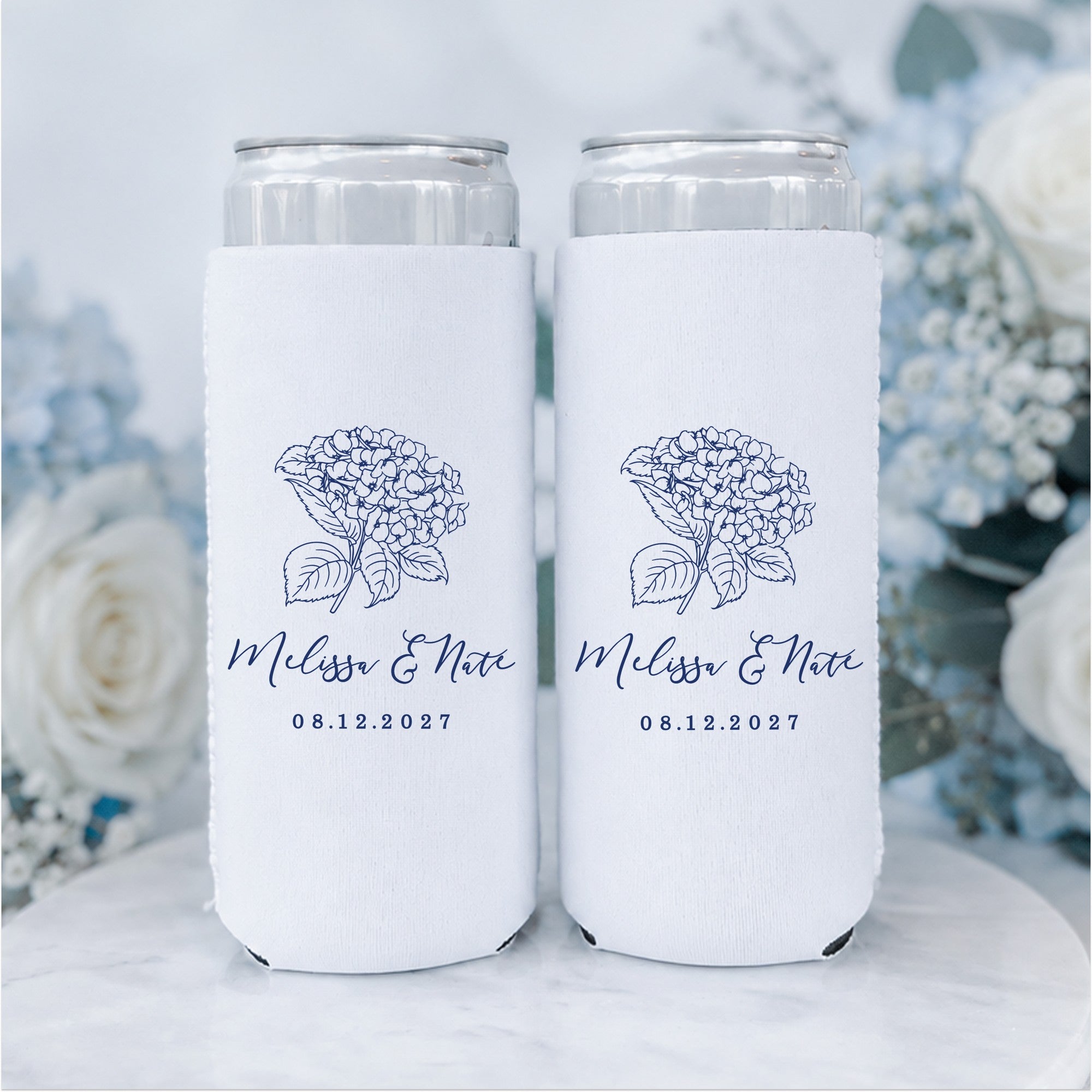 Two white fabric slim can koozies featuring a navy blue outline illustration of a hydrangea flower, perfect for keeping beverages cold at a wedding or special event.