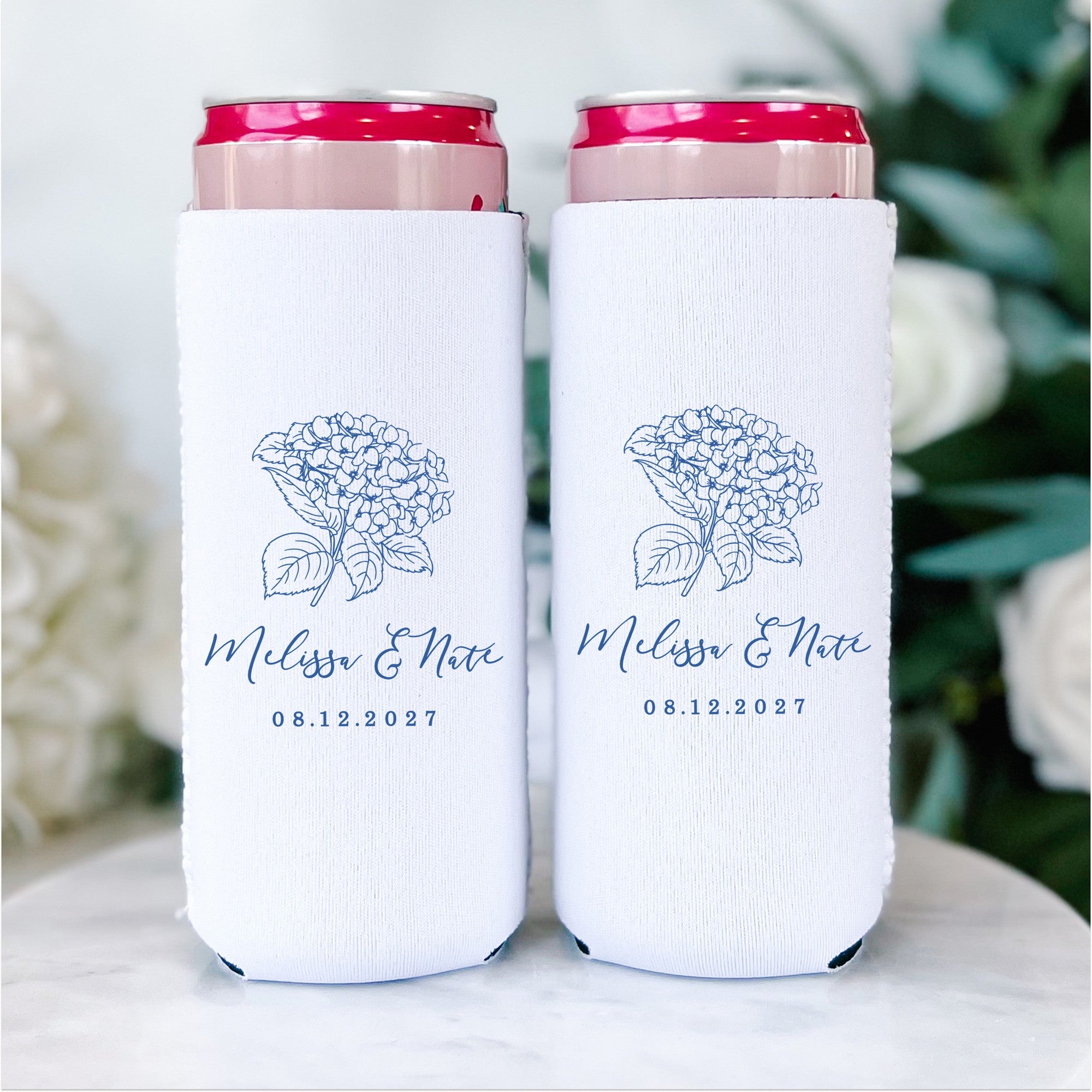 Two white neoprene slim can koozies, designed for a wedding, feature an elegant blue hydrangea floral print to keep beverages chilled.
