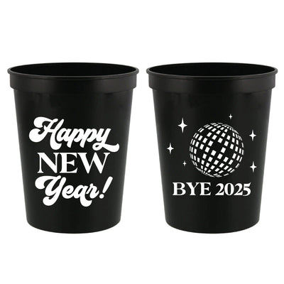 Two black plastic party cups for a New Year's Eve celebration, with one featuring white script text and the other a white disco ball graphic with stars.