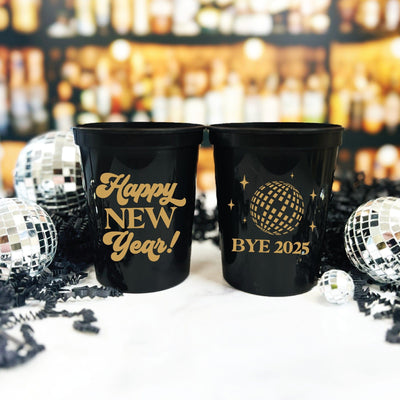 A pair of black plastic party cups featuring festive gold designs with a disco ball motif, perfect for a New Year's Eve celebration.
