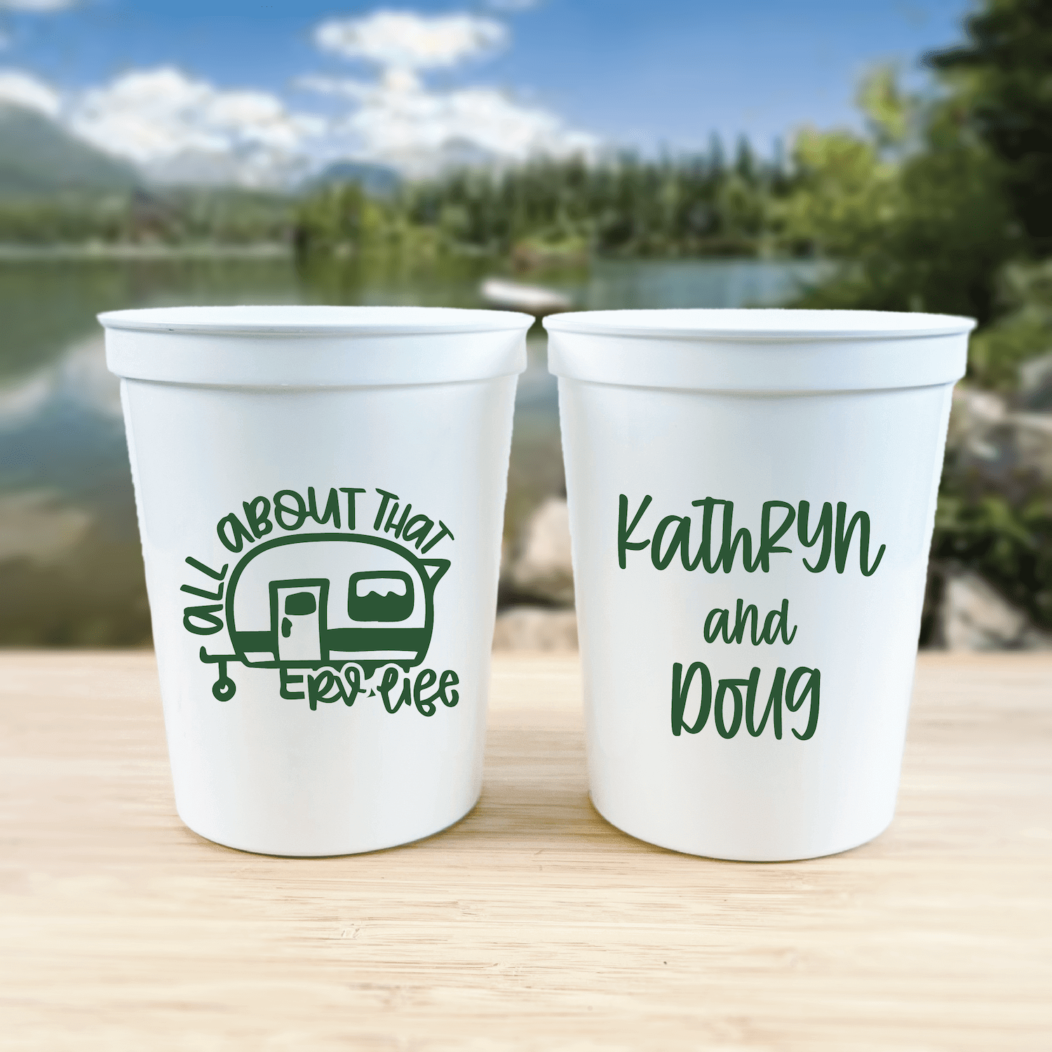 White stadium cups with green text, one showing RV camper design and "All About That RV Life," the other personalized with "Kathryn and Doug"