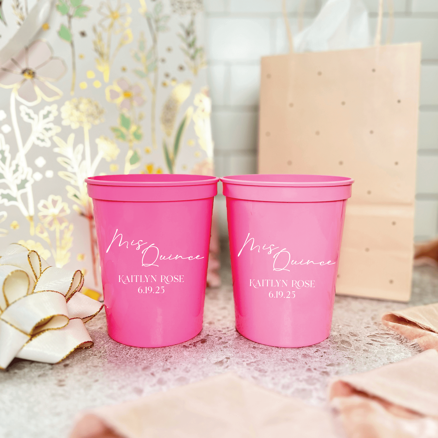 Hot pink stadium cups with "Mrs Quince" and personalized names and date printed in white script text, displayed on sparkly surface with floral decor.