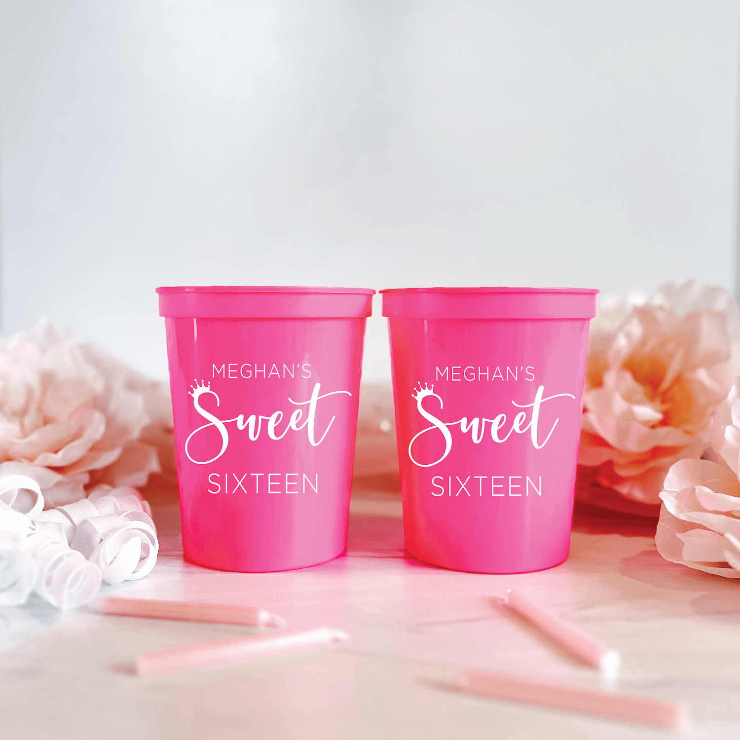 Bright pink stadium cups personalized with "Meghan's Sweet Sixteen" in white script lettering, displayed with decorative flowers and pink straws.