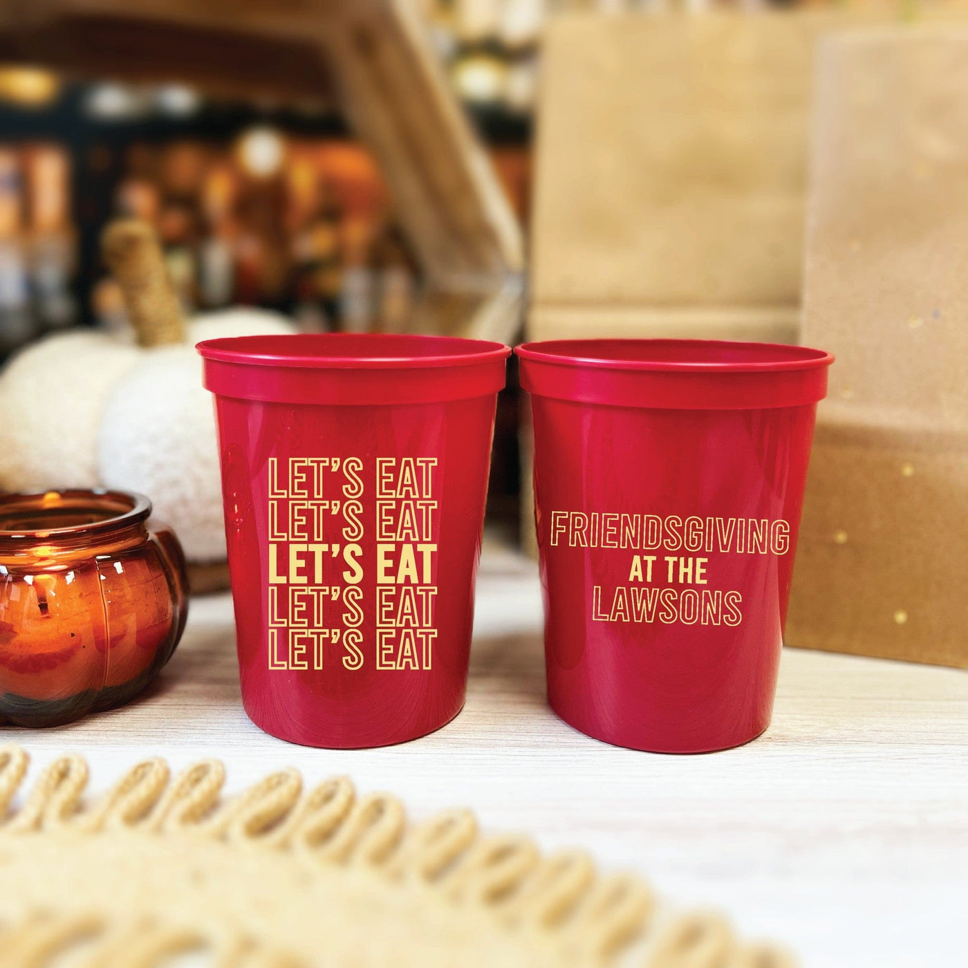 Two personalized red plastic cups with custom gold-colored designs are displayed on a white wooden surface, perfect for a fall-themed event or casual gathering.