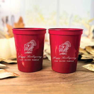 Two vibrant red personalized plastic cups featuring a white outline graphic of a turkey, suitable for Thanksgiving celebrations or fall event decor.