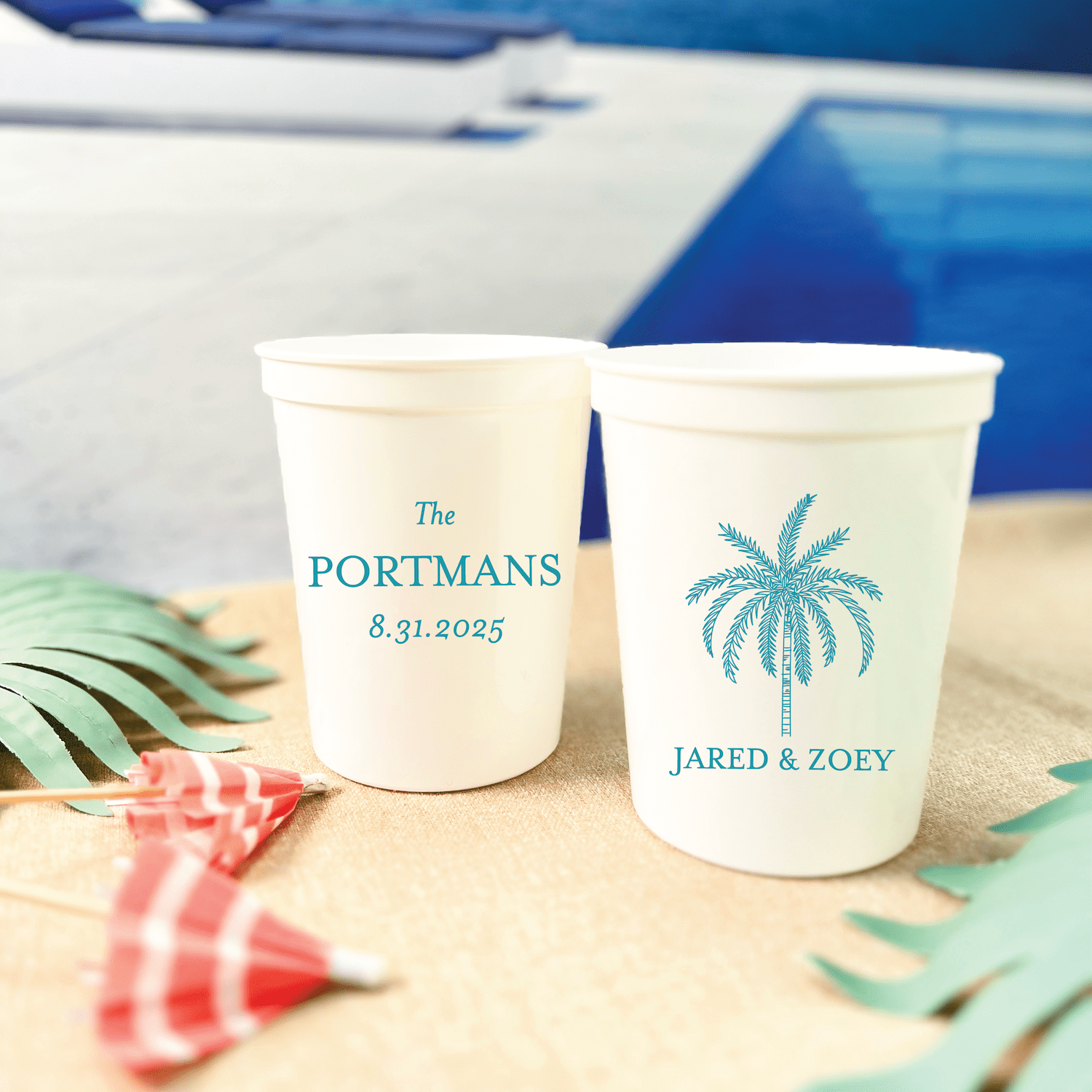 Two white stadium cups personalized with "The Portmans 8.31.2025" and "Jared & Zoey" with a blue palm tree design on sand.