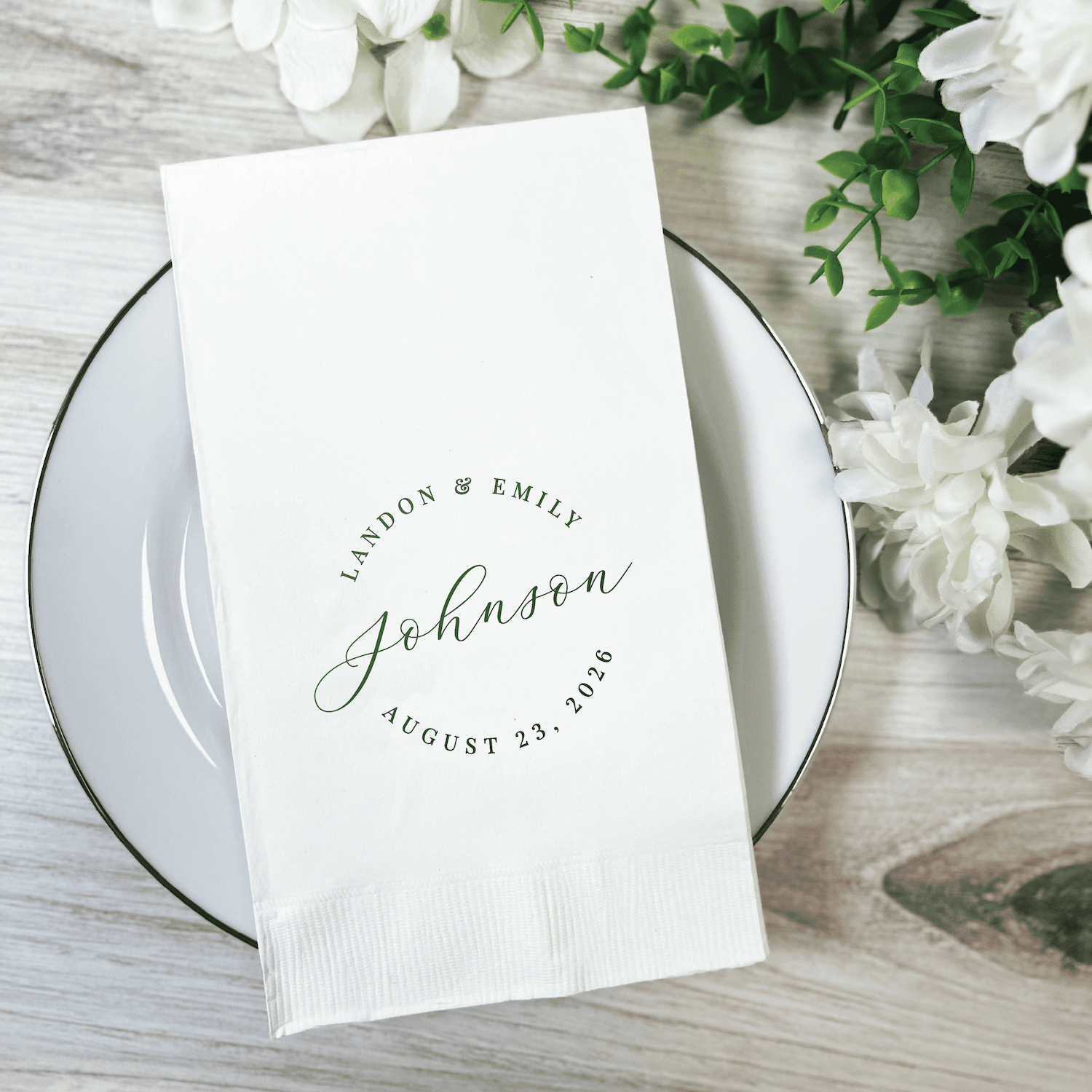 White napkin with "Johnson" and wedding date printed in elegant script on white plate with flowers
