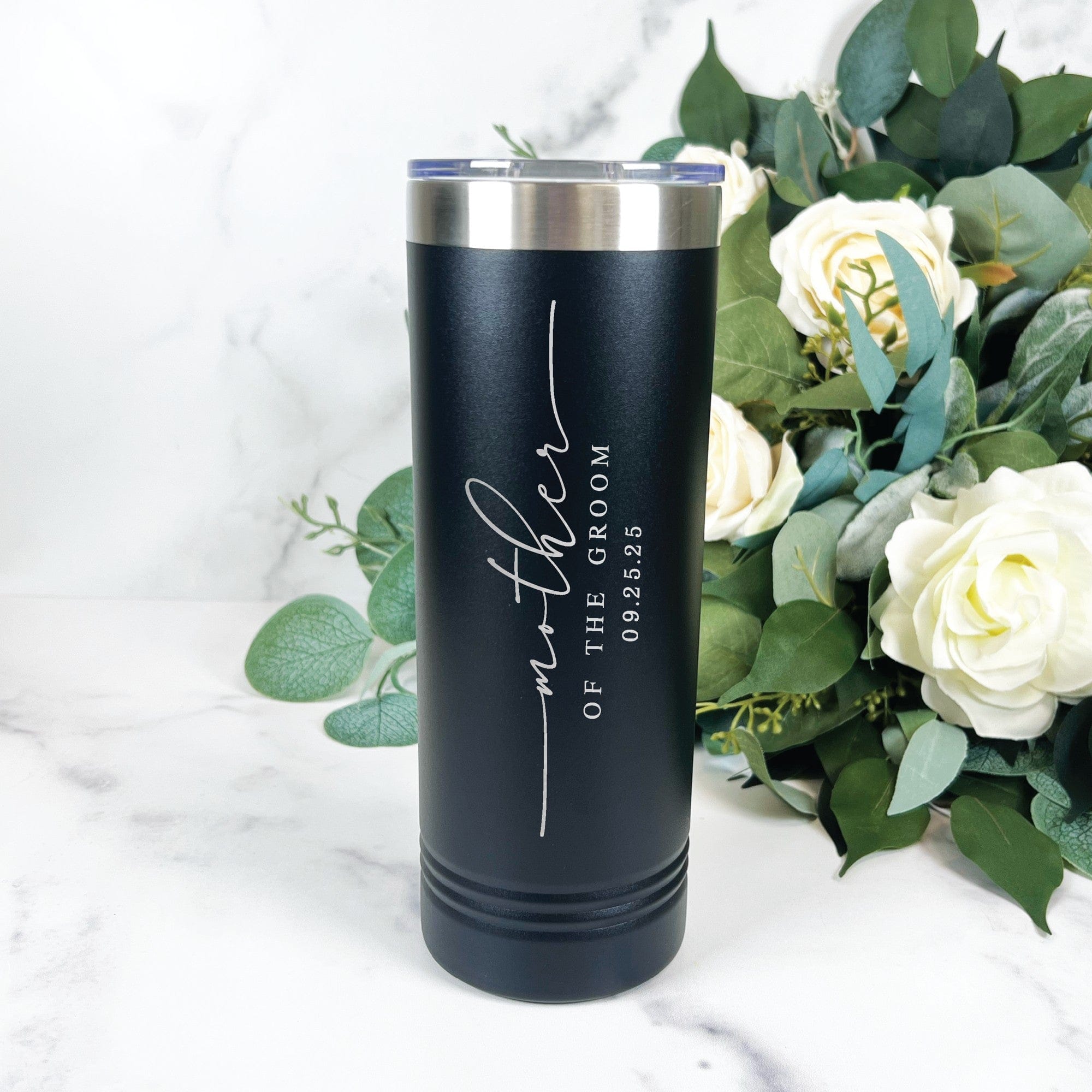 A black insulated stainless steel tumbler with a silver rim and clear lid, featuring elegant custom white engraving, displayed on a marble surface next to a bouquet of white roses and green foliage, ideal for wedding party gifts.
