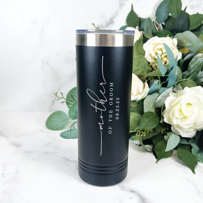 A black insulated stainless steel tumbler with a silver rim and clear lid, featuring elegant custom white engraving, displayed on a marble surface next to a bouquet of white roses and green foliage, ideal for wedding party gifts.