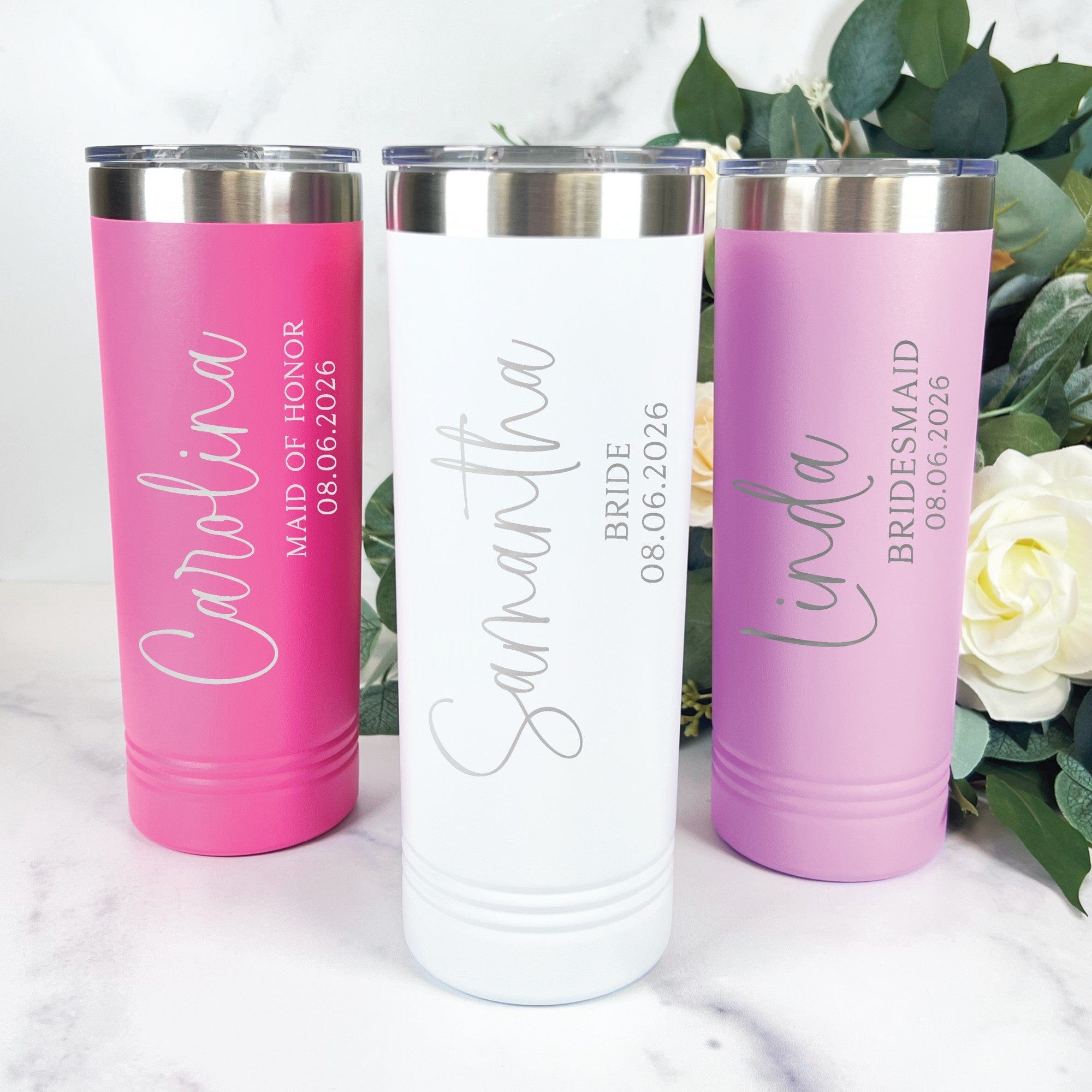 Three personalized stainless steel tumblers in hot pink, white, and lavender colors are displayed, designed as thoughtful wedding party gifts.
