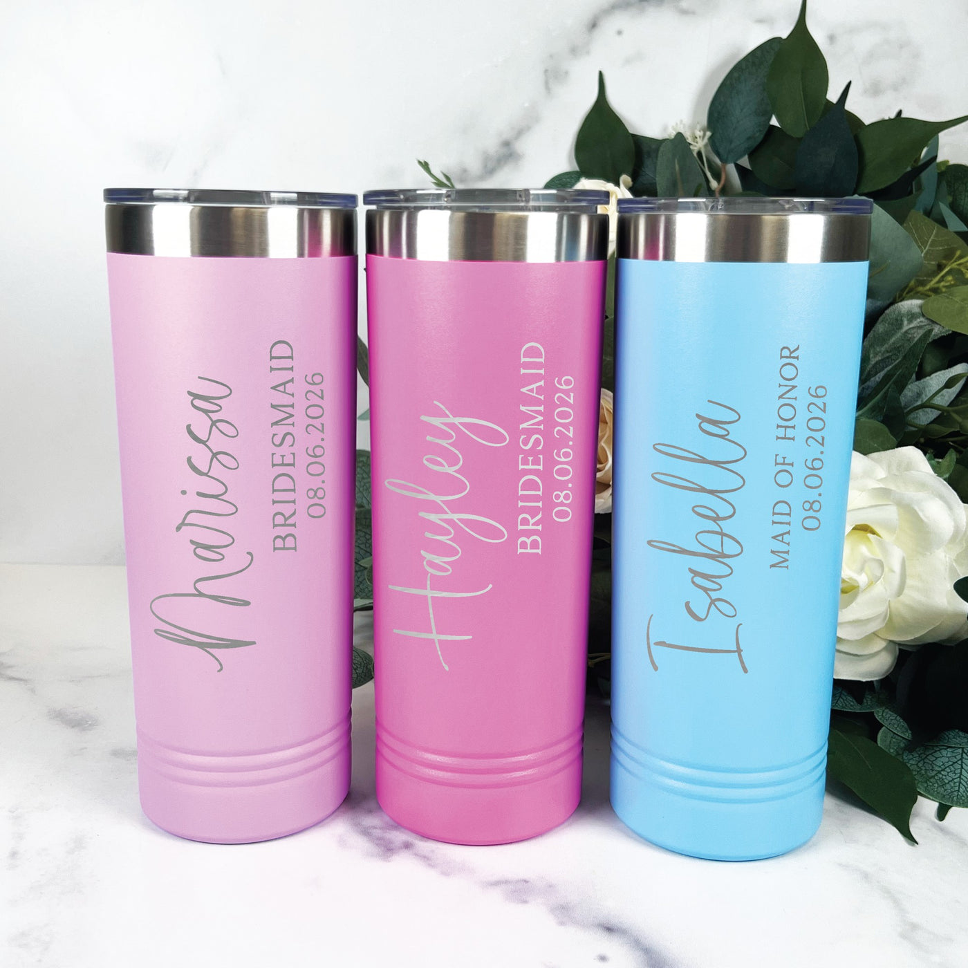 Three personalized insulated stainless steel tumblers, two pink and one light blue, are displayed as thoughtful bridal party gifts for a wedding, each featuring custom laser-engraved text.