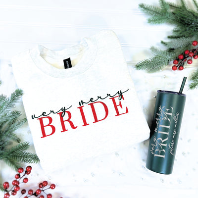 A light gray crewneck sweatshirt and a dark green insulated tumbler with a straw, both featuring a festive bridal-themed design, presented as a personalized Christmas gift set.