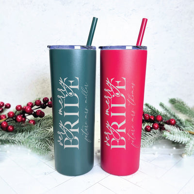 A pair of festive red and dark green insulated tumblers, each with a clear lid and matching straw, featuring personalized white lettering in script and block fonts, perfect for a Christmas bridal celebration.