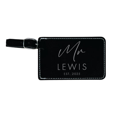 A black faux leather luggage tag with contrasting white stitching and a silver metal buckle, designed for travel or as a wedding and event favor.