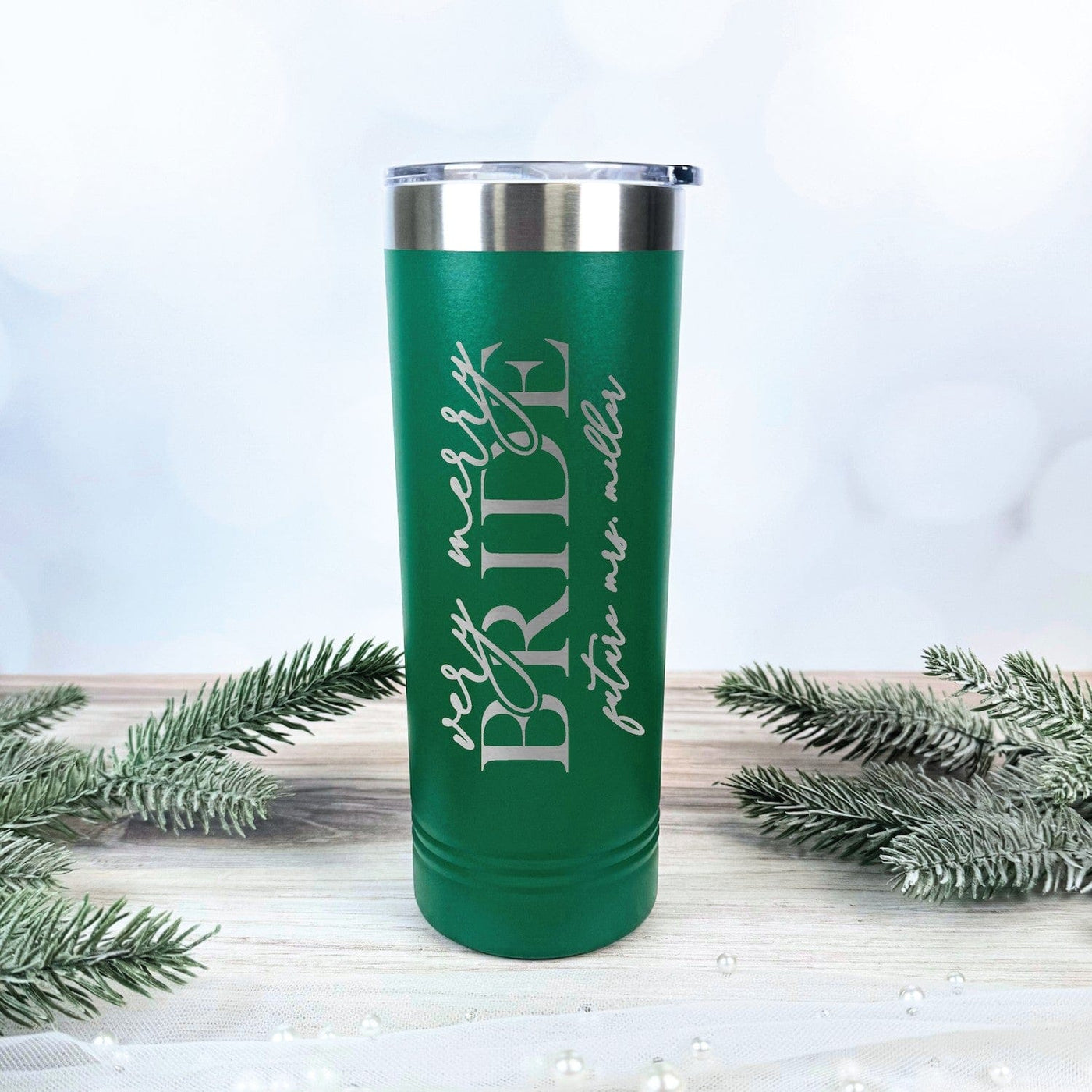 A tall, green insulated metal tumbler with a silver lid, custom-engraved for a bridal celebration with a festive holiday theme.