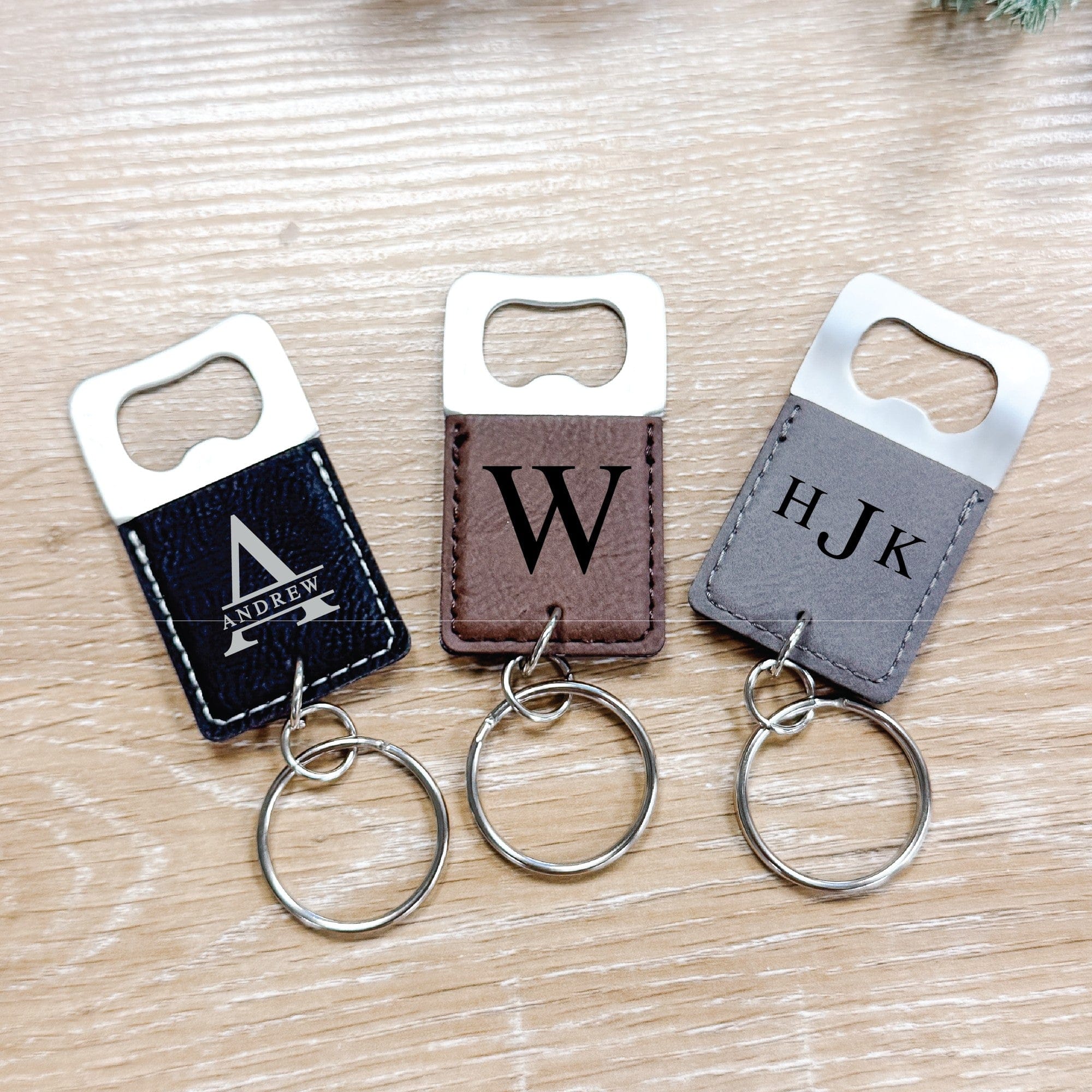 A trio of personalized bottle opener keychains, featuring a metal opener and a textured faux leather handle in dark blue, brown, and grey, designed as practical and elegant event favors.